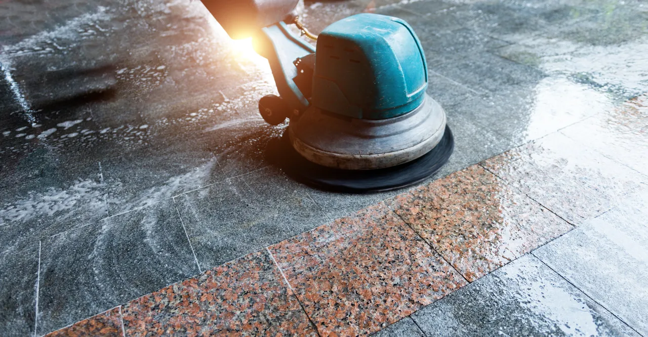 A rotary floor machine cleaning a stone surface